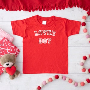 Puede incluir: Camiseta roja con texto blanco que dice "LOVER BOY" en una fuente de estilo universitario.