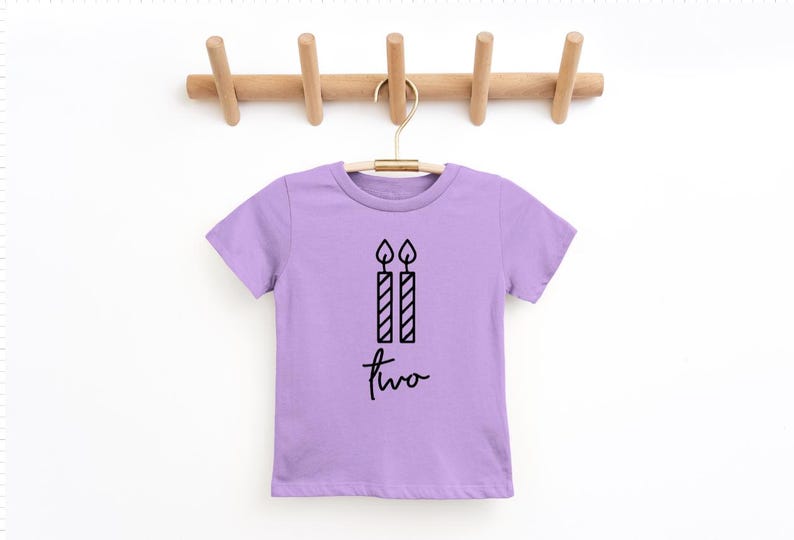 May include: A lavender short-sleeved t-shirt with a black graphic of two birthday candles and the word "two" written in cursive.