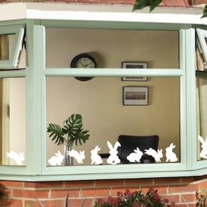May include: A bay window with a green frame and white bunny silhouettes on the glass. The window is open and there is a plant in a pot on the windowsill.