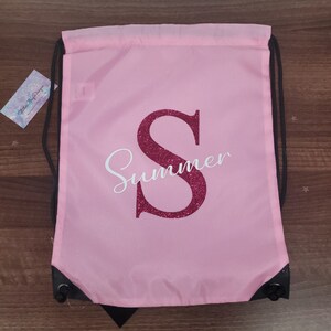May include: Pink drawstring bag with a large sparkly pink letter "S" and the word "Summer" in white cursive lettering.