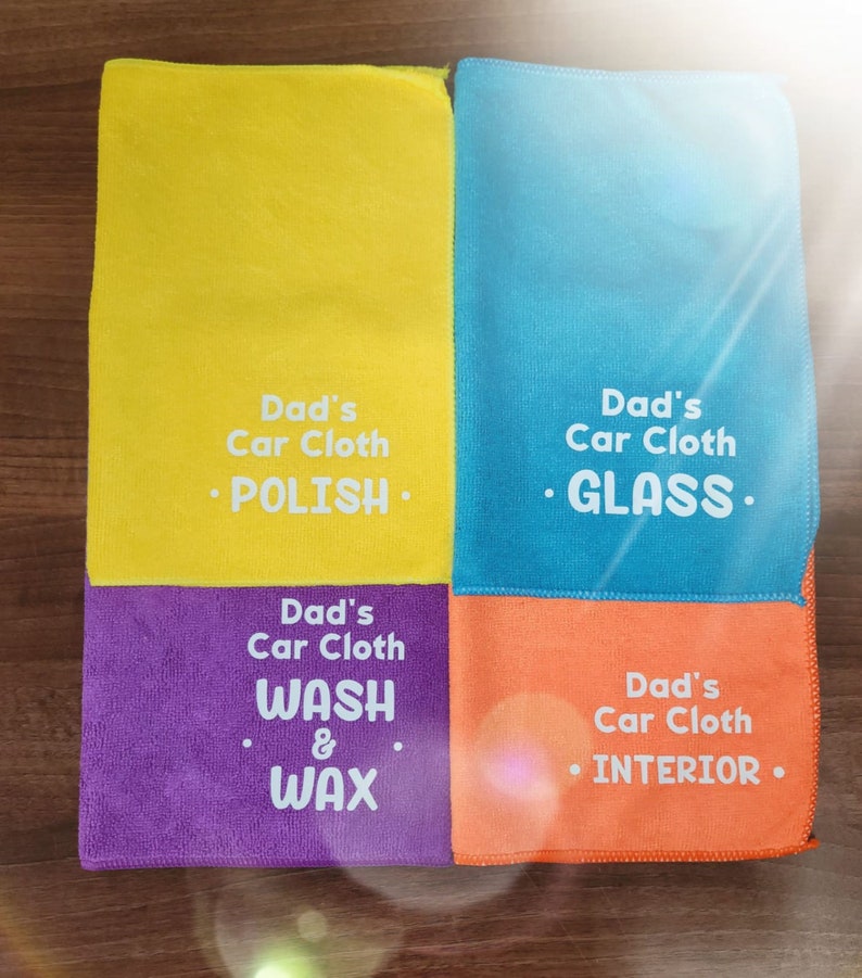 May include: Four microfiber cloths in yellow, blue, purple, and orange with white text. The text reads "Dad's Car Cloth" followed by a cleaning task: "POLISH", "GLASS", "WASH & WAX", and "INTERIOR".