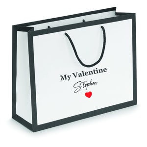 May include: White gift bag with black trim and handles. The bag has the text "My Valentine Stephen" with a red heart.