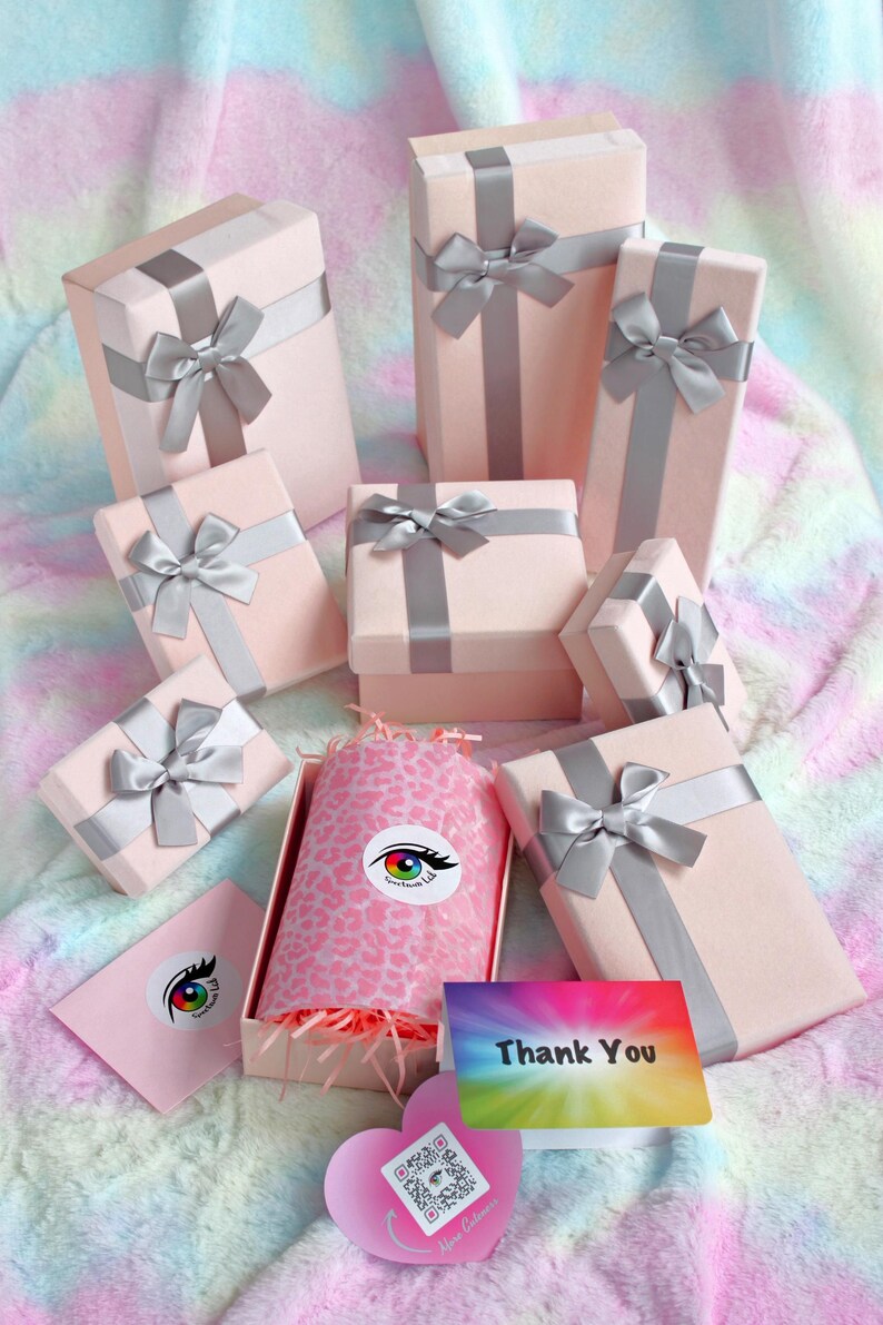 May include: A collection of light pink gift boxes wrapped with silver satin ribbons and bows. One open box contains pink leopard print tissue paper and shredded filler. Includes a thank you card and a heart-shaped card with a QR code.