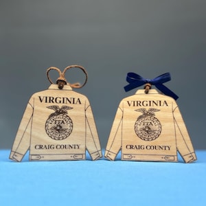May include: Two wooden ornaments shaped like jackets. Each ornament has the word "VIRGINIA" at the top and "CRAIG COUNTY" at the bottom. The ornaments feature a detailed FFA emblem. One has a brown string, the other a blue ribbon.