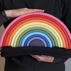 Puede incluir: Un juguete de arco de madera de colores arcoíris con 12 piezas, sostenido por las manos de una persona. El juguete está hecho de madera natural y está pintado en una variedad de colores, incluyendo rosa, rojo, naranja, amarillo, verde, azul y morado.