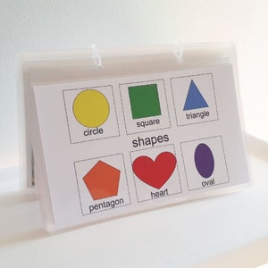 May include: A white card with colorful shapes and their names: circle, square, triangle, pentagon, heart, and oval. The card is labeled "shapes" at the top.