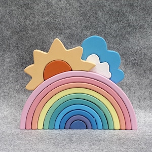 May include: A rainbow-colored wooden arch toy with a yellow sun and a blue cloud on top. The arch is made of 10 pieces that can be stacked and nested.