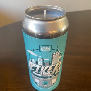 May include: A blue and white candle in a can with the text "Castle Island" and "Five Island IPA" on the label. The candle is shaped like a can of beer.