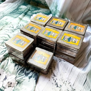 Può includere: Una collezione di scatole di metallo quadrate vintage con un'etichetta dorata e gialla raffigurante una scena storica. Le scatole sono impilate in più pile, mostrando il loro aspetto metallico invecchiato. Le etichette hanno uno schema di colori blu, rosso e bianco.