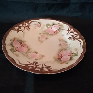May include: A large, white ceramic bowl with a brown rim and floral design. The bowl features pink roses and green leaves painted on the white surface.