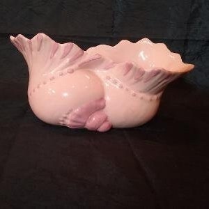 May include: A pink ceramic planter shaped like a seashell with ruffled edges. The planter has a smooth, glossy finish and is decorated with raised dots.