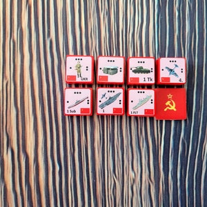 Könnte beinhalten: Rote und weiße Spielsteine mit verschiedenen militärischen Einheiten, darunter Infanterie, Panzer, U-Boote und Flugzeuge. Die Steine sind mit Zahlen und Abkürzungen beschriftet, z. B. "1 Tk" für einen Panzer und "1 Sub" für ein U-Boot. Ein roter Stein mit einem Hammer-und-Sichel-Symbol ist ebenfalls sichtbar.