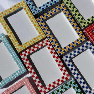 Puede incluir: Una colección de marcos de fotos rectangulares con bordes de mosaico hechos de pequeñas baldosas cuadradas en varios colores, incluyendo amarillo, azul, rojo, verde, rosa y azul claro, rodeando un área central rectangular blanca.
