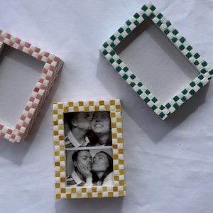 Puede incluir: Tres marcos de fotos decorativos con diseños de mosaicos tejidos. Un marco es amarillo y blanco, que muestra dos fotos en blanco y negro. Los otros dos marcos están vacíos, uno rosa y blanco, el otro verde y blanco. Todos los marcos son rectangulares.