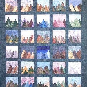 May include: A patchwork quilt featuring a repeating mountain landscape design. Each square showcases a different color palette, with shades of blue, green, brown, and purple. The quilt is made of fabric squares arranged in a grid pattern, creating a textured and visually appealing piece.