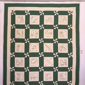 May include: A handmade quilt with a green and cream color scheme. The quilt features a repeating pattern of embroidered squares with simple line drawings depicting various scenes. The border is cream with a green edge.