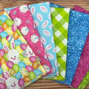 Może przedstawiać: Kolekcja kolorowych tkanin o tematyce wielkanocnej. Wzory obejmują pisanki, króliki, owce, ślady łap, kratę vichy i wzory bąbelków. Tkaniny są w odcieniach różu, niebieskiego, zielonego, żółtego i fioletowego, idealne do wiosennych rzemiosł i dekoracji.