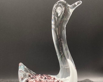 May include: A clear glass swan figurine with a white and purple speckled design. The swan's neck is curved and its head is tilted slightly to the side.