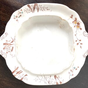 Puede incluir: Un plato de servir de porcelana blanca con un diseño floral marrón y verde. El plato tiene un pozo de forma cuadrada en el centro.