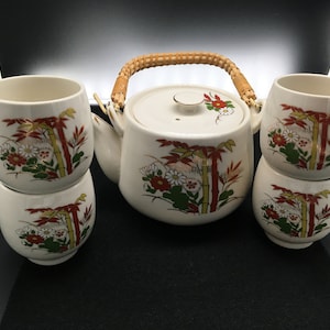 May include: A white ceramic teapot with a bamboo and floral design and a woven handle, along with four matching teacups.