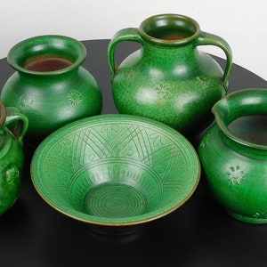 Puede incluir: Un conjunto de cinco piezas de cerámica verde, que incluyen un tazón, una jarra y tres jarrones. Las piezas están decoradas con un sencillo patrón floral y tienen un aspecto rústico y hecho a mano.