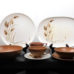 Op de afbeelding: Een set vintage bruin en wit serviesgoed met een tarwe patroon. De set bevat twee grote ovale serveerschalen, twee bruine kommen en twee bruine theekopjes met schoteltjes.