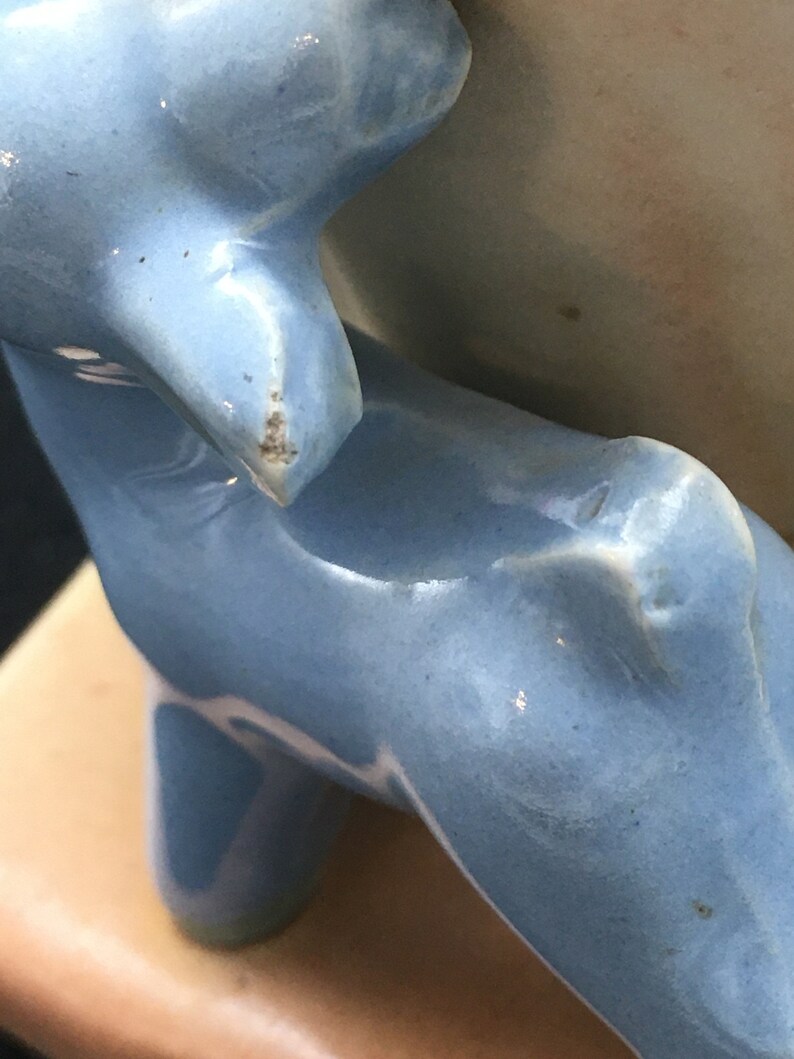 May include: A blue ceramic figurine of a dog, with a chipped ear, standing on a pink base.