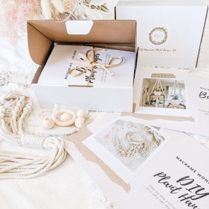 May include: A DIY macrame plant hanger kit with instructions, rope, wooden beads, and a wooden ring. The kit is packaged in a white box with the text "DIY Macrame Plant Hanger Kit" on the front.