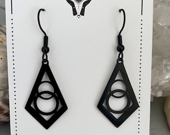 Brincos pendentes minimalistas com formato geométrico preto e círculos.