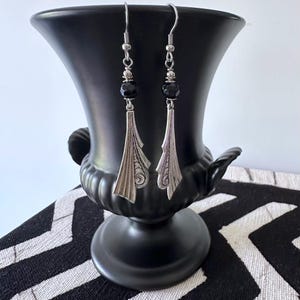 Op de afbeelding: Zilveren oorhangers met zwarte kralenaccenten. De oorbellen hebben een geometrisch ontwerp met een waaiervorm.