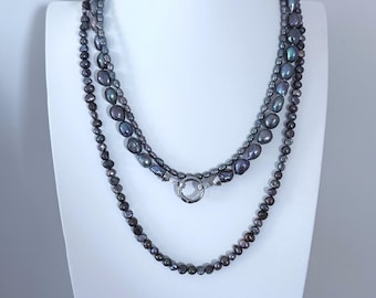 Può includere: Una collana a più fili con perle grigio scuro, iridescenti e di forma barocca di varie dimensioni. I fili sono collegati da una chiusura circolare in metallo color argento. Le perle presentano una lucentezza metallica e sono disposte a strati.