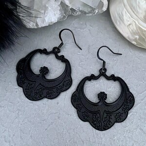 Pu&ograve; includere: Un paio di orecchini neri in filigrana. Ogni orecchino presenta un design traforato ornato con motivi floreali e a volute. Gli orecchini hanno una chiusura a gancio e una finitura opaca.