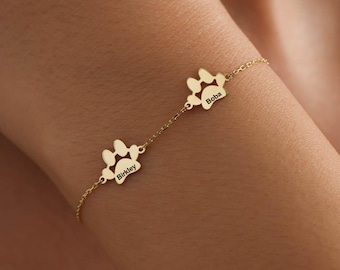 May include: Gold chain bracelet with two paw print charms, each engraved with a dog's name: Bailey and Bella.