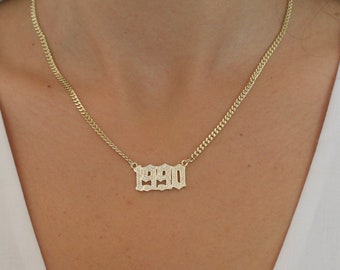 May include: A gold chain necklace with a pendant that says "1990" in a gothic font.