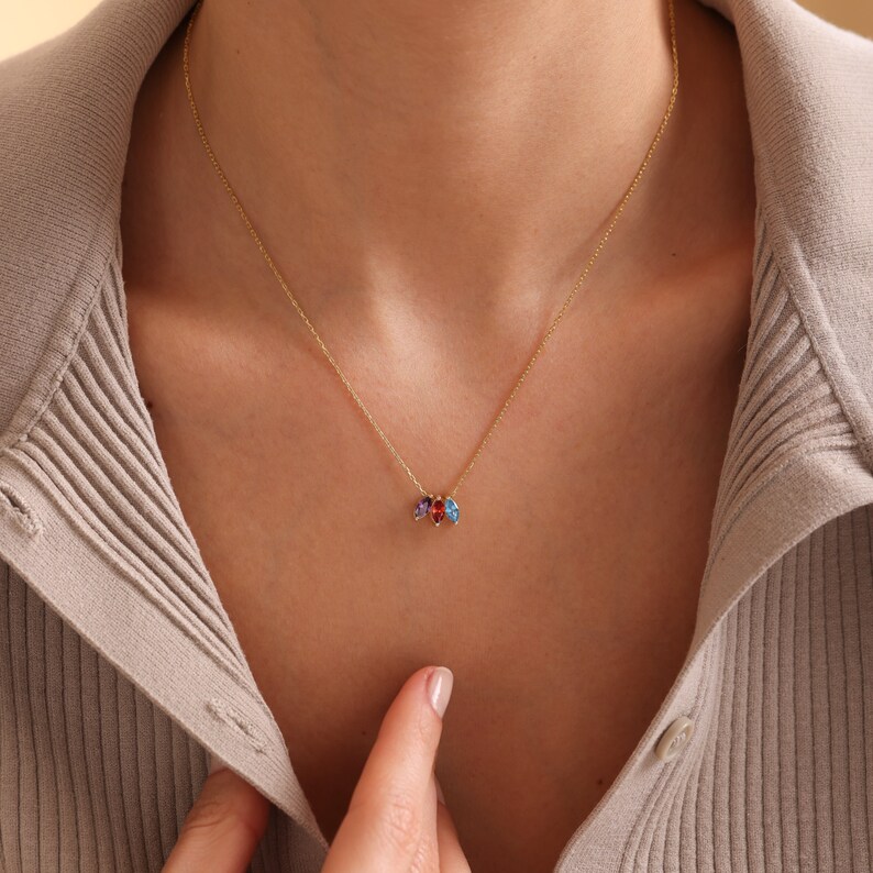 Pu&ograve; includere: Una collana con catena d'oro con un piccolo ciondolo con tre pietre preziose colorate. Le pietre preziose sono rossa, blu e viola.