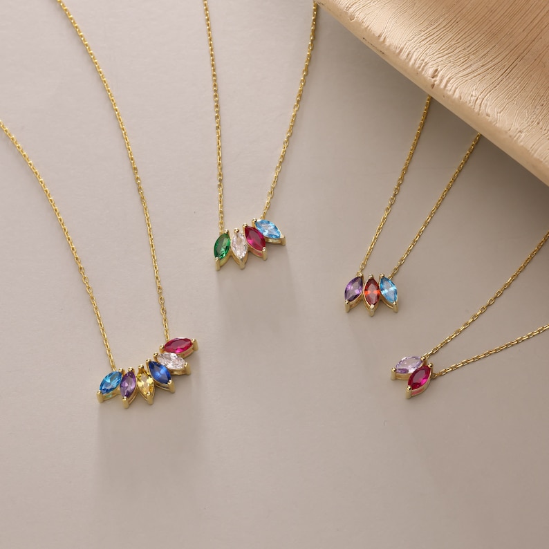 Pu&ograve; includere: Cinque collane d'oro con ciondoli di pietre preziose di diversi colori. Ogni ciondolo presenta una fila di pietre a forma di marquise di diversi colori, tra cui blu, verde, rosso, viola e giallo.