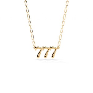 Pu&ograve; includere: Una collana color oro con il numero "777" come ciondolo. Il ciondolo &egrave; in un carattere stilizzato ed &egrave; attaccato a una delicata catena con maglie rettangolari. La collana &egrave; posta su uno sfondo bianco.