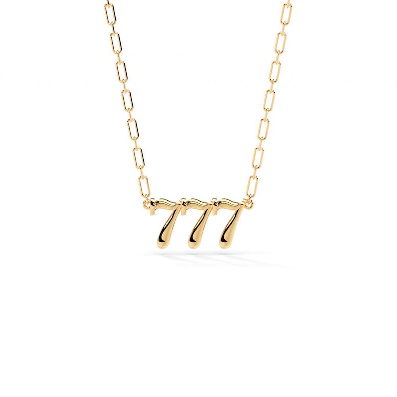 Pu&ograve; includere: Una collana color oro con il numero "777" come ciondolo. Il ciondolo &egrave; in un carattere stilizzato ed &egrave; attaccato a una delicata catena con maglie rettangolari. La collana &egrave; posta su uno sfondo bianco.