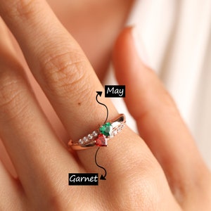 Pode incluir: Anel de ouro rosa com uma pedra de granada vermelha e uma esmeralda verde. O anel &eacute; adornado com pequenos diamantes brancos. O anel &eacute; etiquetado como "Granada" e "Maio".