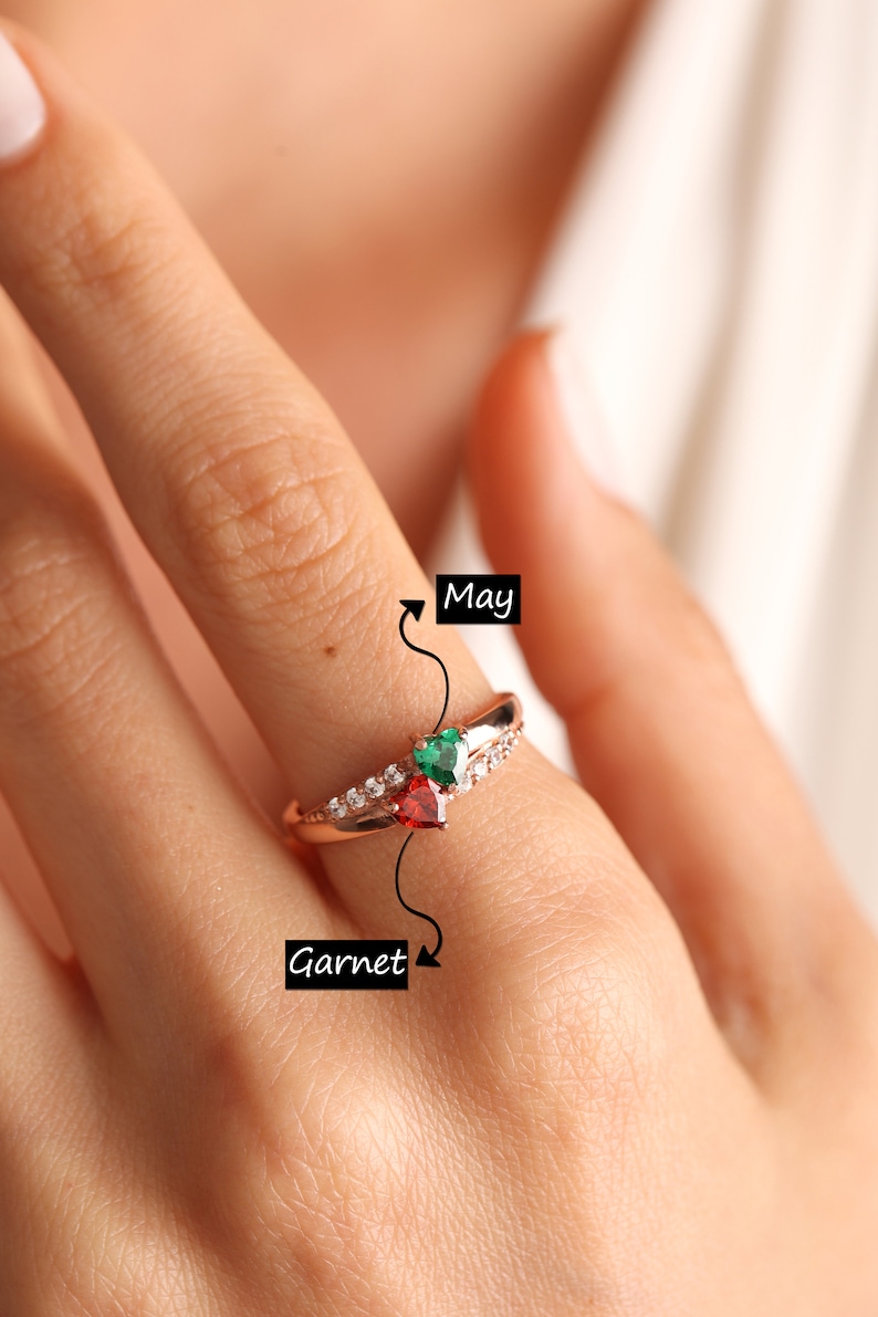 Pode incluir: Anel de ouro rosa com uma pedra de granada vermelha e uma esmeralda verde. O anel &eacute; adornado com pequenos diamantes brancos. O anel &eacute; etiquetado como "Granada" e "Maio".