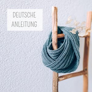 May include: A teal blue crocheted scarf draped over a wooden ladder with the text "DEUTSCHE ANLEITUNG" on a white wall.