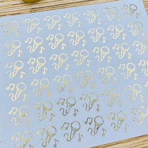 May include: A sheet of gold sticker decals with a repeating pattern of microphones and musical notes. The stickers are on a white background.