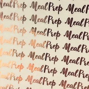 May include: A sheet of white paper with multiple gold foil stickers that say "Meal Prep" in a handwritten font.