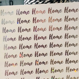 May include: A sheet of white sticker paper with the word "Home" repeated 15 times in a holographic silver font.