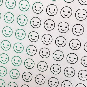 May include: A sheet of white paper with a gradient of green and black smiley face stickers. The stickers are arranged in a grid pattern.