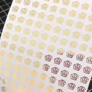 May include: A sheet of white paper with a repeating pattern of gold and burgundy gift boxes. The boxes are outlined in gold and filled with a burgundy color.