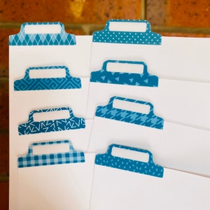 May include: Eight blue patterned paper tabs with a white rectangular space for writing. The tabs have different patterns including polka dots, geometric shapes, and a plaid pattern.