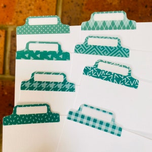 May include: Set of teal blue patterned index tabs with white labels. The tabs have different geometric patterns, including polka dots, diamonds, triangles, and gingham.