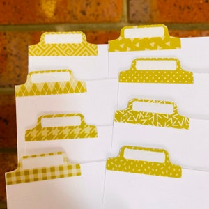 May include: Set of seven yellow patterned index tabs with white labels. The tabs have different patterns, including geometric shapes, polka dots, and stripes.