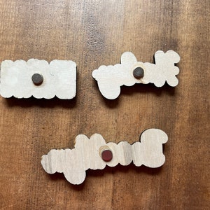 May include: Three wooden signs with the words "Home", "Welcome", and "Blessed" written on them. Each sign has a small black magnet attached to the back.